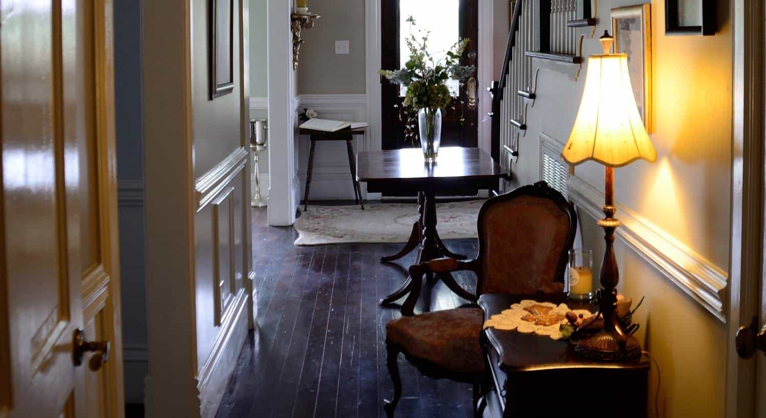 Main entrance interior along stairway with wood flors,, small tables, flowers, lamp, and side chair