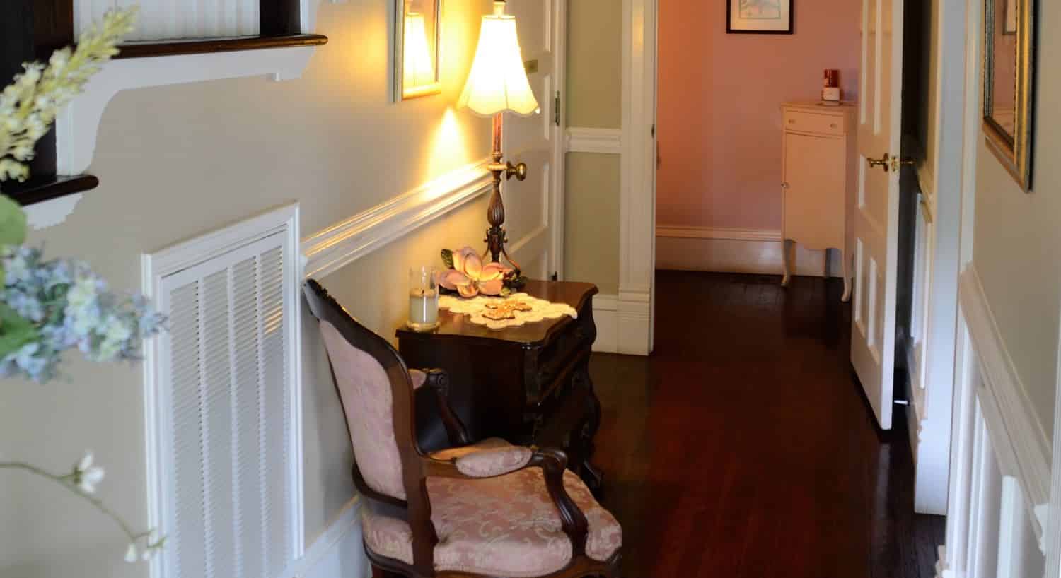 Front interior hallway along stairway with wood floor, side chair and table with lamp