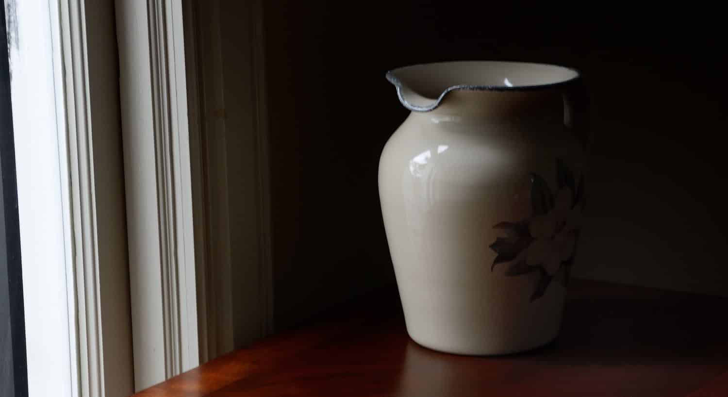 Large white vase sitting on a wood table next to a window