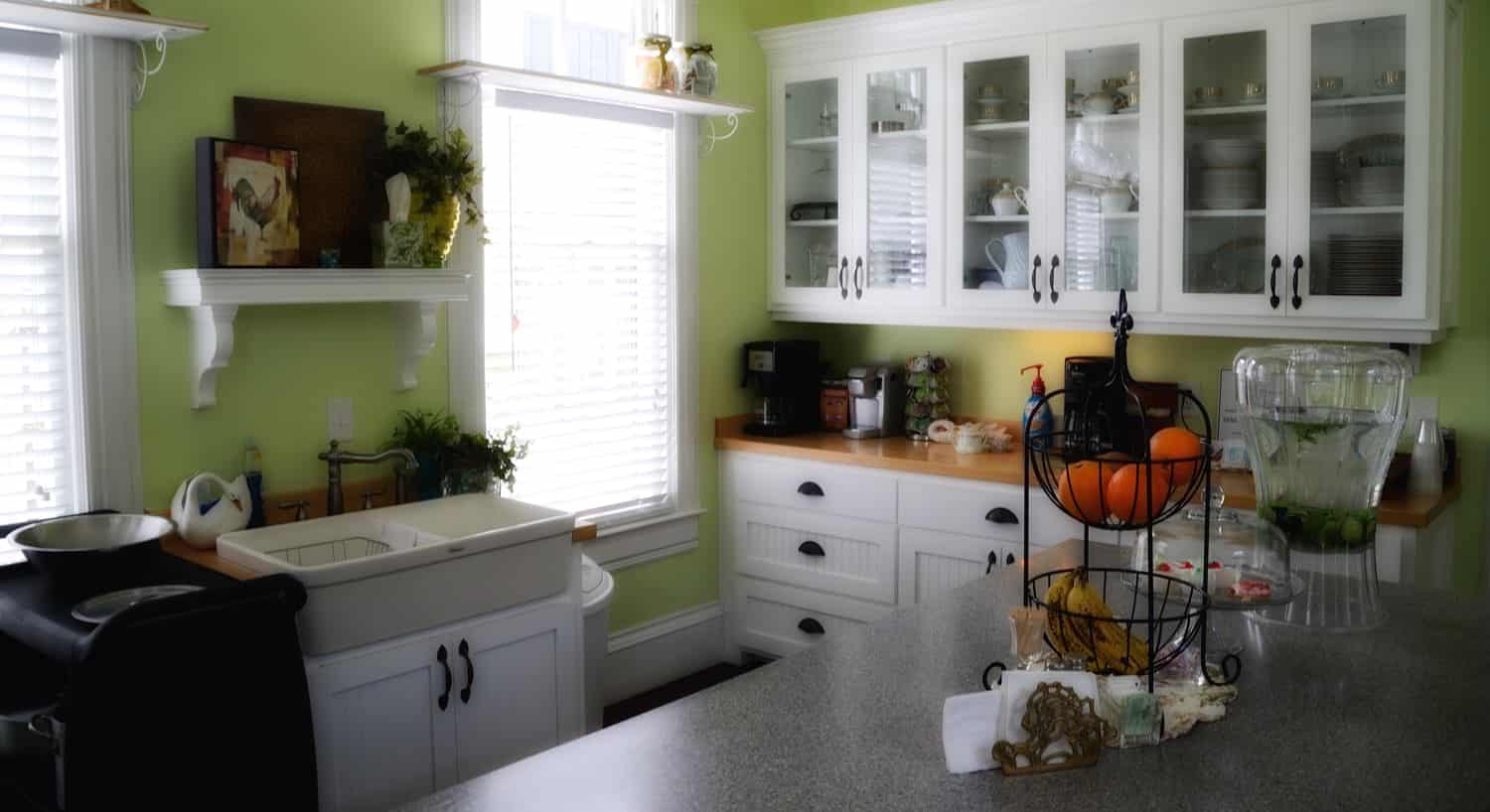 Kitchen with light green walls, white cabinets and shelves, wood tops, two windows and center island
