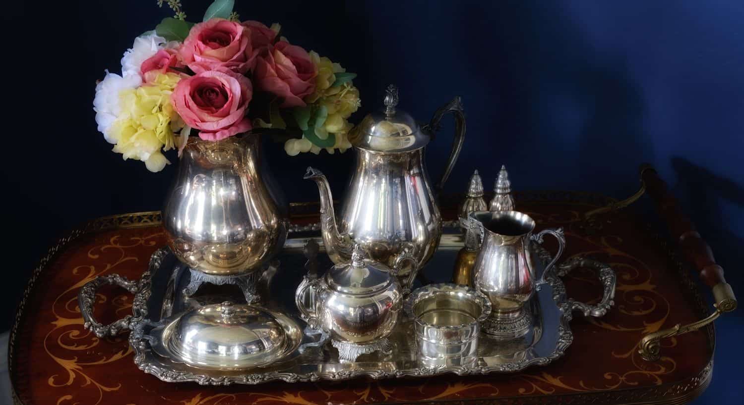 Silver tea set on a silver tray next to vase of fresh pink, yellow, and white flowers