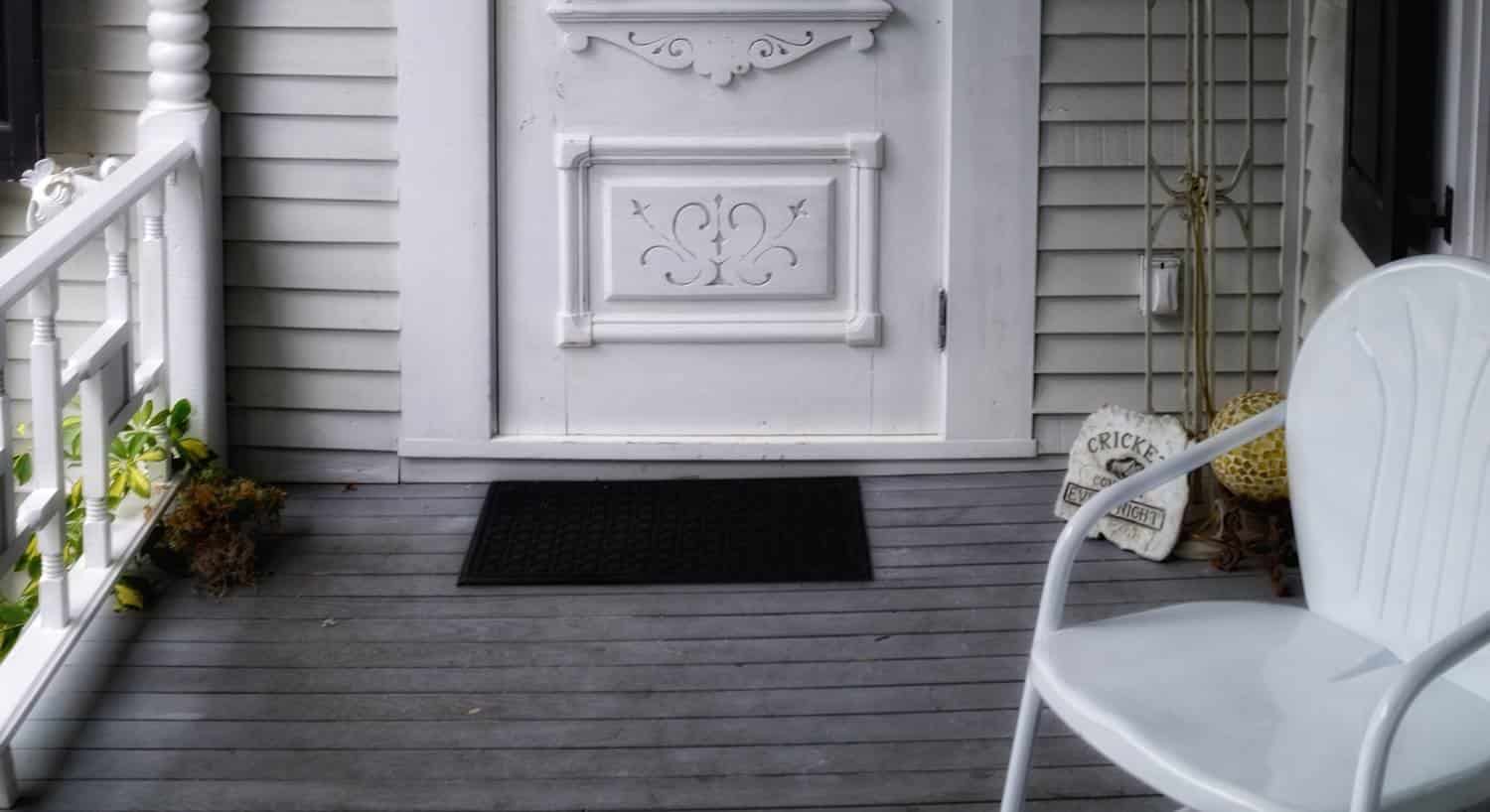 Covered porch with white railing, white chair and white entry door
