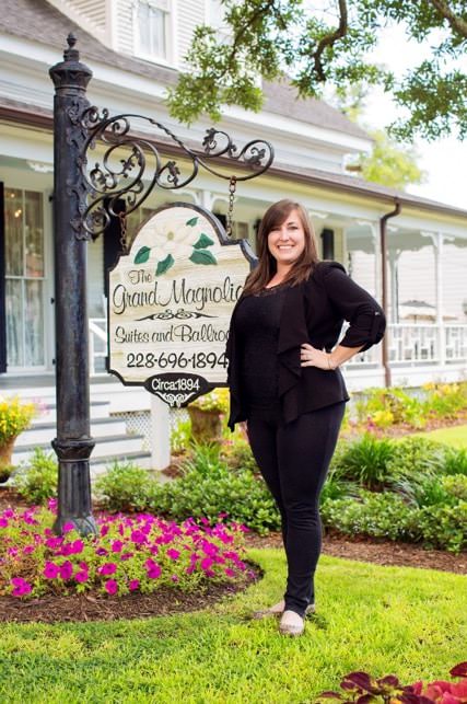 Lady dressed in black standing in front of Grand Magnolia sign surrounded by flowers