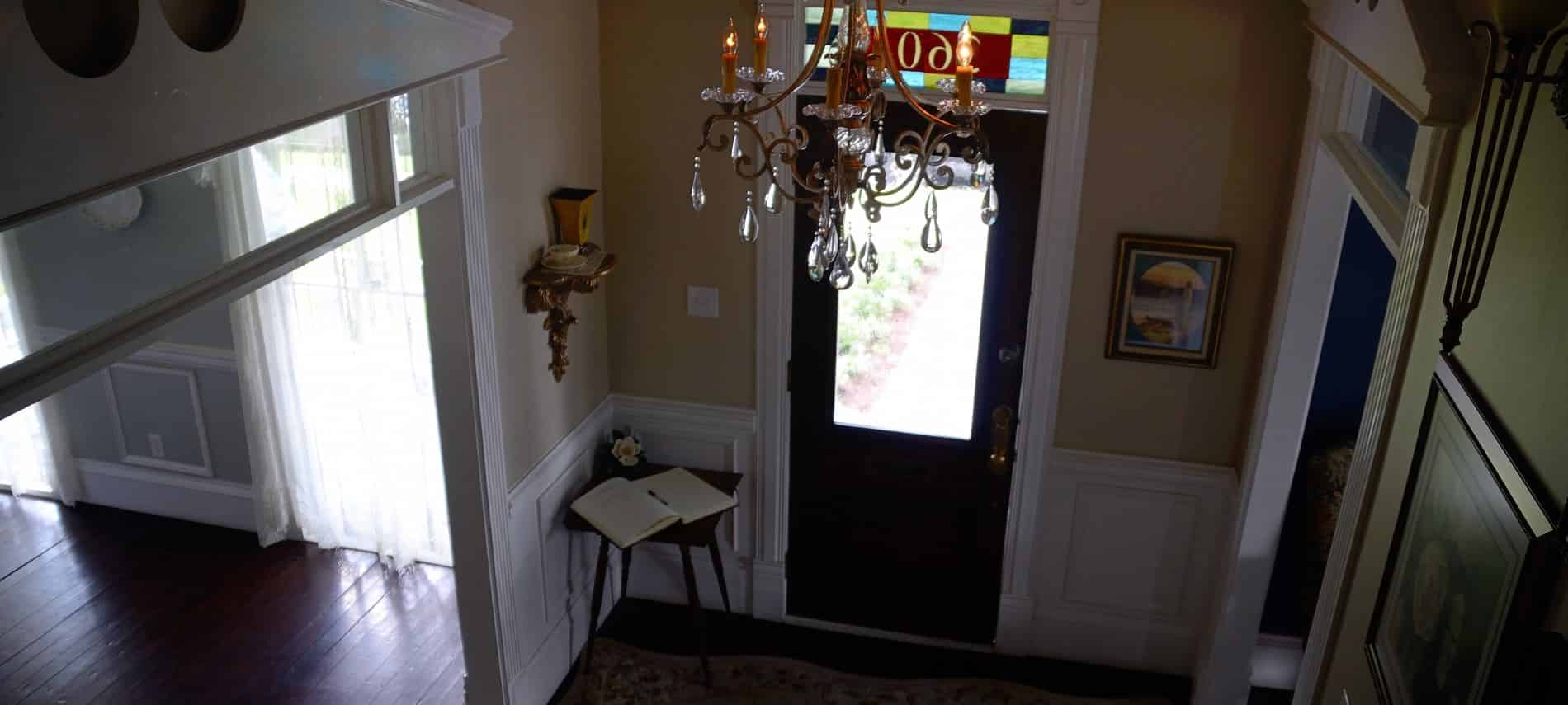 Main entrance foyer with glass door, cased openings, white wainscoting, and elegant brass and crystal chandelier