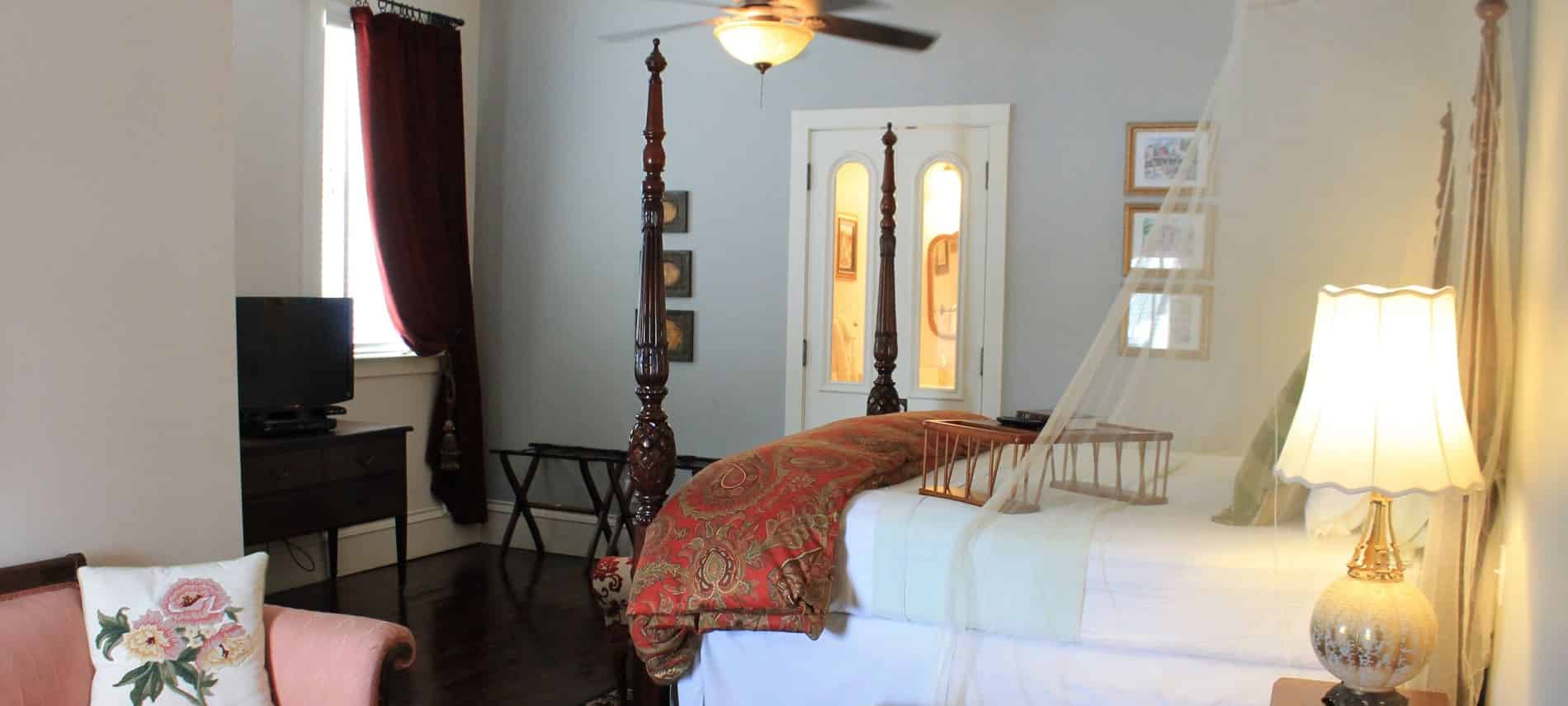 Savannah guest room with window, dark wood four poster bed, sheer white canopy panels and guest bath