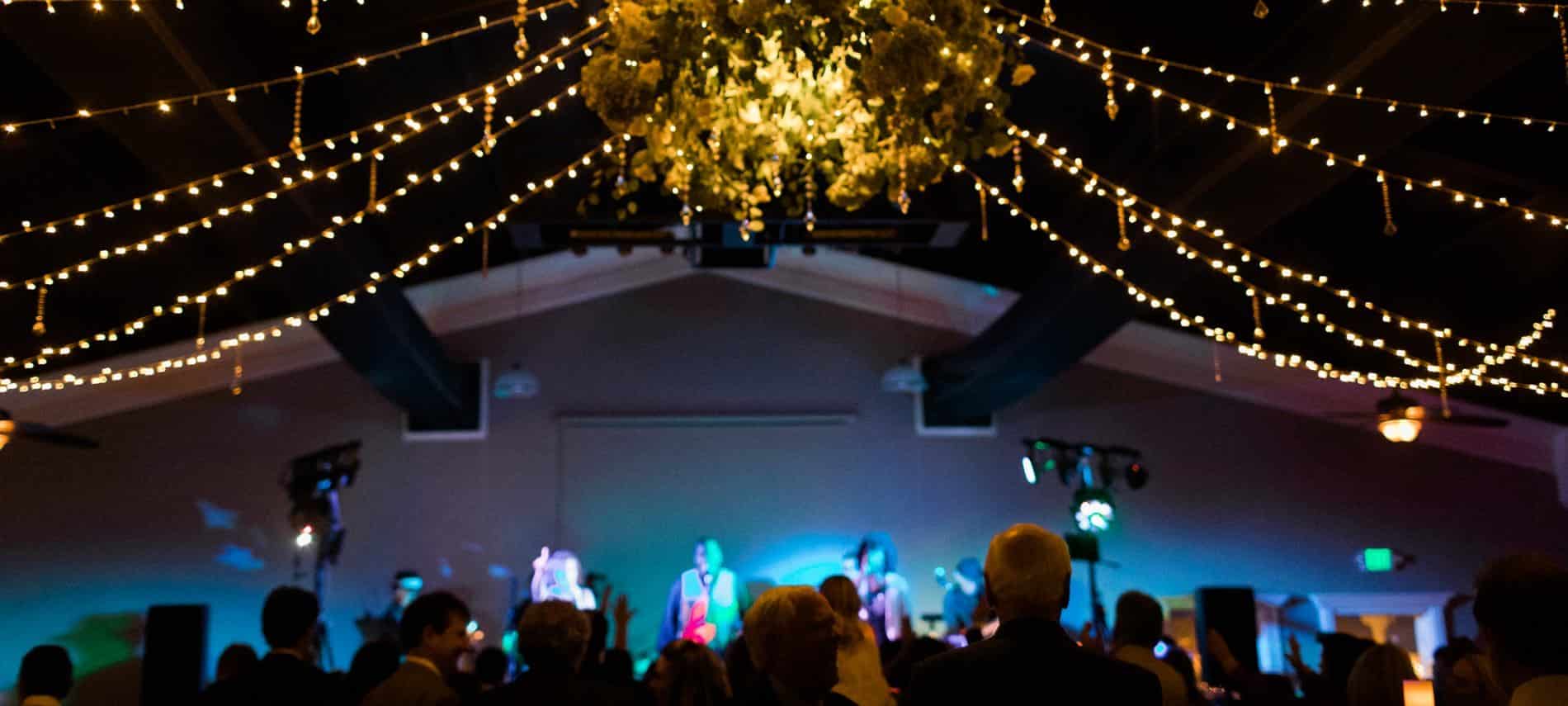 Wedding celebration at night with twinkle light ropes overhead and a stage with colorful lights