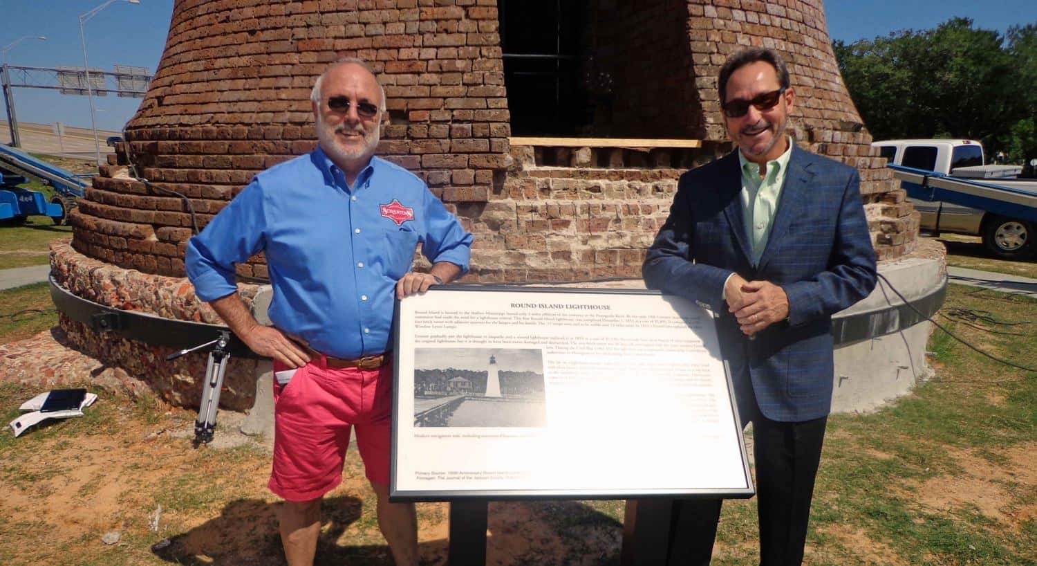 Two men standing on each side of the sign in front of the lighthouse
