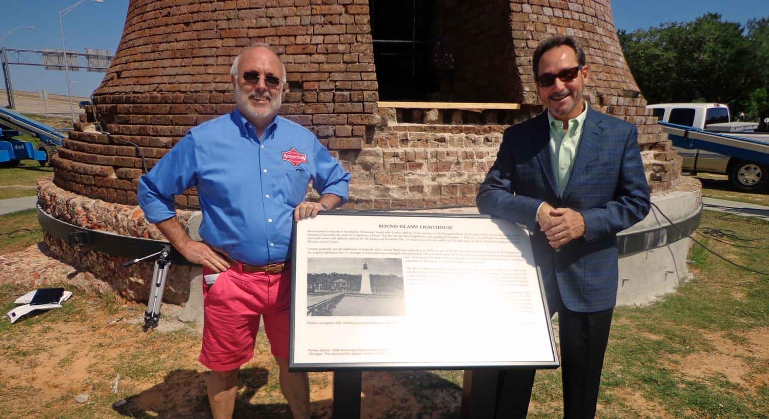 Two men standing on each side of the sign in front of the lighthouse