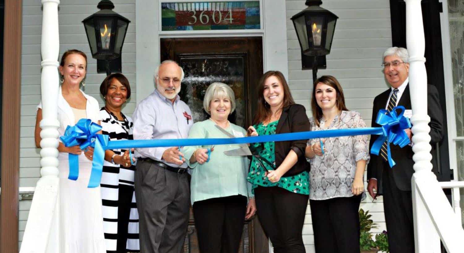 The owners and several others on the front porch getting red to cut the ribbon at the opening ceremony