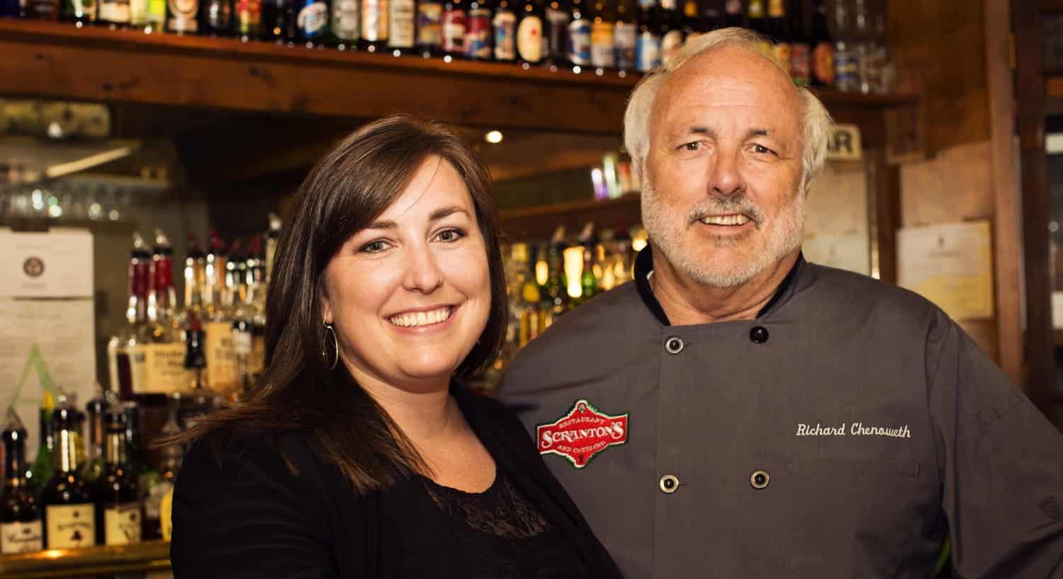 Owners standing in front of a bar with man different bottles