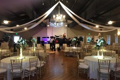 Ballroom draped with white fabric starting from the crystal chandelier with white linen tables and chivari chairs.