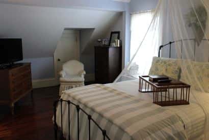 Cape Cod guest room with light blue walls, metal bed with striped bedding and sheer white canopy overhead