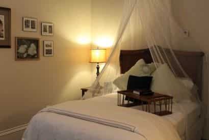 Charleston guest room, bed with tall wood headboard and sheer white canopy, nightstand with lamp, and white bedding