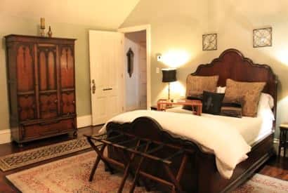 New Orleans guest room vaulted ceiling, dark scalloped wood bed, white bedding, nightstands with lamps and tall armoire