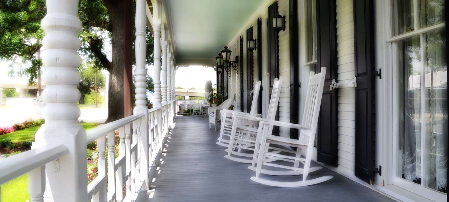 Long covered porch with windows, black shutters, painted wood floor, white railing, posts and rocking chairs