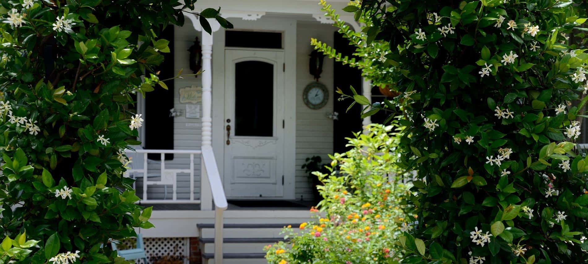 Entrance of Grand Magnolia with steps leading up to covered front porch with white railing and door visible through lush greenery