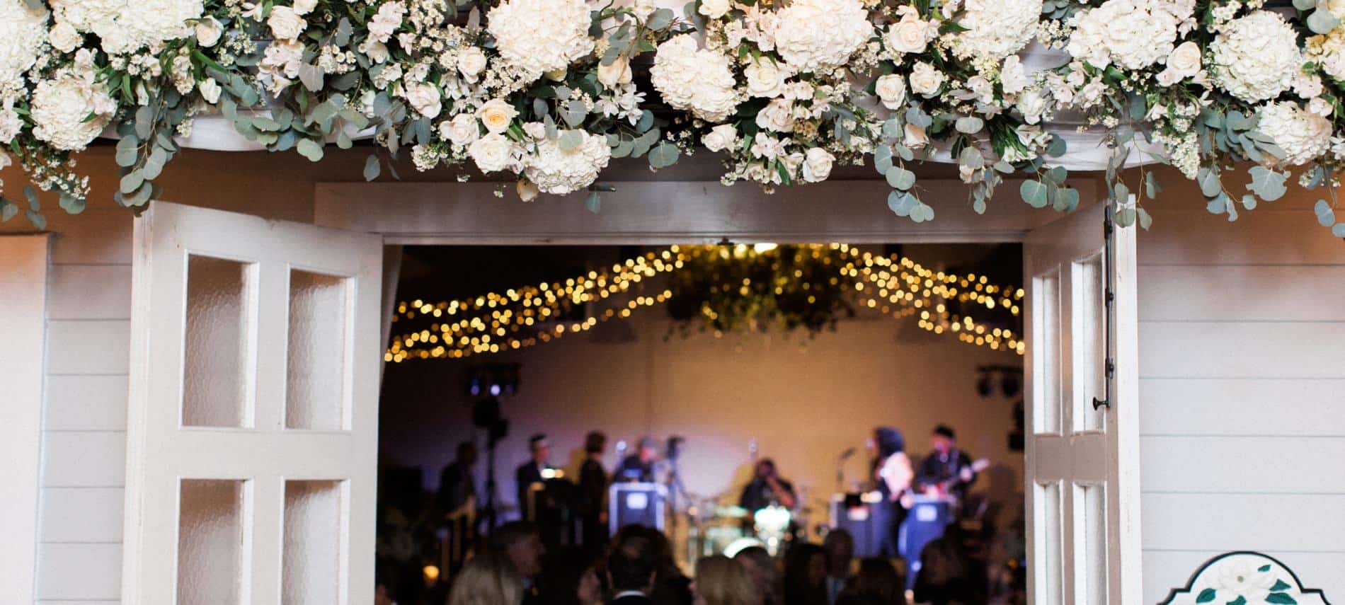 Double French doors swung open with white flowers overhead and view of wedding band inside