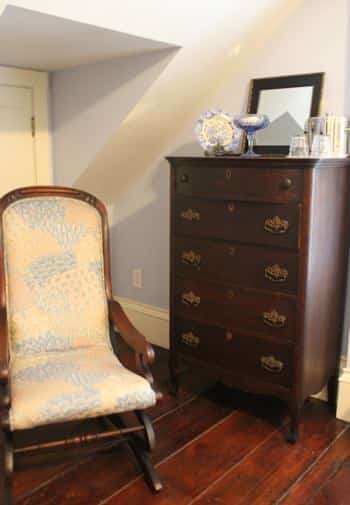 Cape Cod guest room with wide plank floors, slanted ceiling, dresser and rocking chair with cushions