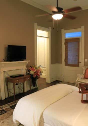 Garden guest room with tan walls, wood floors, bed with white bedding, ceiling fan, upholstered chair and TV