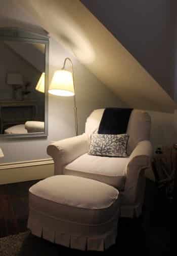 Key West guest room with slanted wall, upholstered chair and ottoman, wall mirror and floor lamp