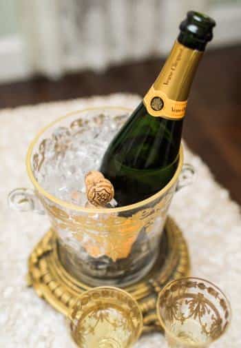 Bottle of champagne chilling in a gold and glass bucket with two gold and glass flutes nearby