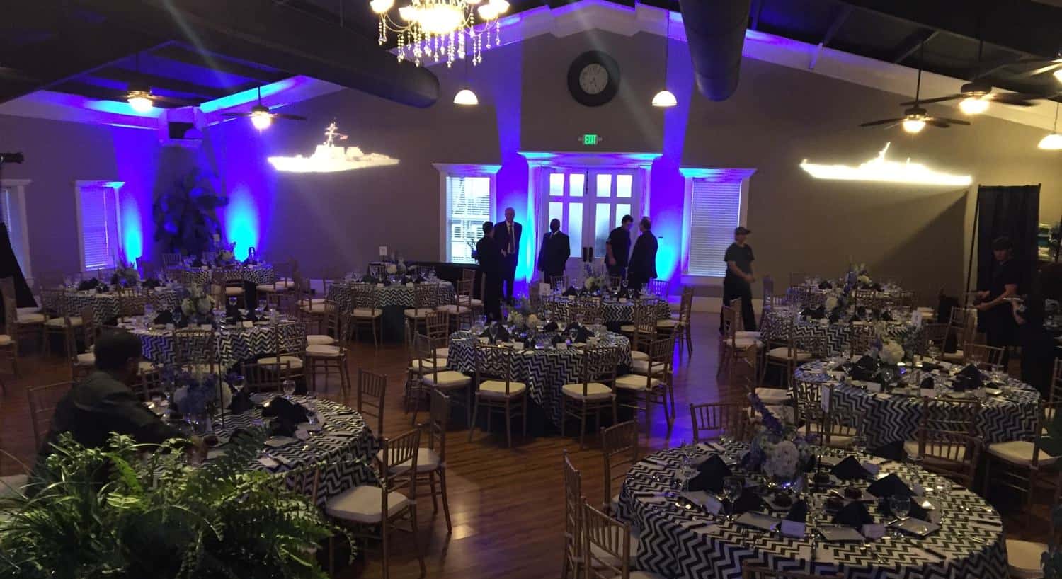 Ballroom decorated with round tables and chairs, black and white tablecloths, and blue lights